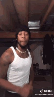 a man wearing a white tank top and a black beanie is dancing .