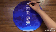 a person is painting the moon phases on a blue circle
