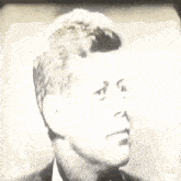 a black and white photo of a man in a suit and tie looking at the camera .