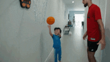 a man in a red nike shirt is playing basketball with a little boy