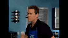 a man wearing a blue apron and a headset is standing in a kitchen .