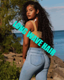 a woman with long curly hair stands in front of a body of water