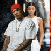 a man in a red hat and a woman in a white tank top are standing next to each other on a street