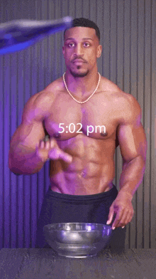a shirtless man standing next to a bowl of water with the time 5:02 pm on the screen