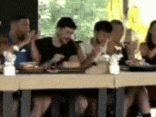 a group of people are sitting at a table with their hands in the air