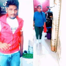 a man in a red vest and a woman in a blue shirt are walking down a hallway .