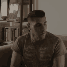 a man is sitting on a couch in front of a bookshelf with a picture of a man on it .