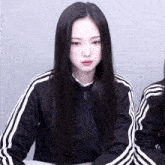 a girl with long black hair wearing a black adidas jacket
