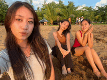 three women are sitting on a sandy beach posing for a photo