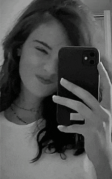 a black and white photo of a woman taking a selfie with her phone .