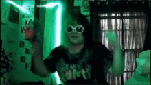 a person wearing sunglasses and a shirt that says ' i am idiot ' on it is dancing in a dark room .