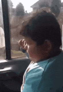 a boy in a blue shirt is looking out of a car window .
