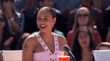 a woman in a pink dress is laughing while sitting in front of a microphone in a crowd .