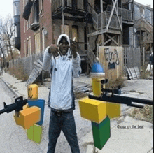 a man is standing on a street holding a gun next to a roblox character .
