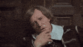 a man with a white collar and a black jacket has his hand on his chin