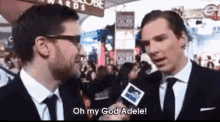 a man in a suit and tie is talking into a microphone and says oh my god adele .