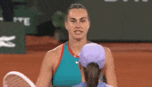 a woman in a purple hat is hugging another woman in a blue shirt on a tennis court .