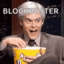 a man in a suit and tie is eating popcorn from a yellow bucket .