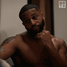 a shirtless man is looking at himself in a mirror with a be it logo in the corner