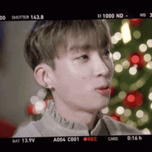 a close up of a person 's face with a red cross on his cheek in front of a christmas tree .