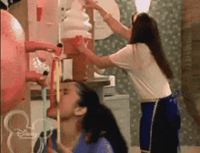 two women are standing next to each other in front of a disney ice cream machine .