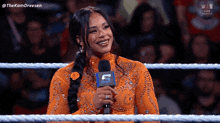 a woman is sitting in a wrestling ring holding a microphone with the number 5 on it .
