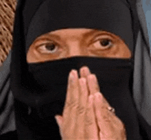 a woman wearing a hijab covering her face with her hands .