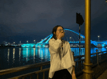 a woman with glasses stands in front of a blue bridge
