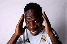 a man in a white adidas shirt is making a funny face while holding his hands to his head .