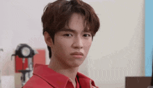 a young man in a red shirt is making a funny face while looking at the camera .