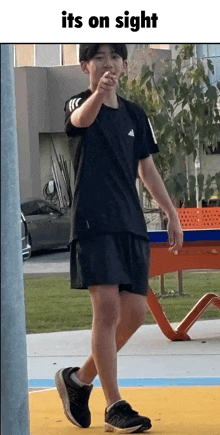 a young man in a black shirt and shorts is pointing at something with the words its on sight above him .