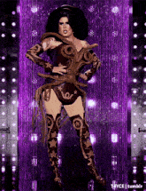 a drag queen is standing in front of a purple curtain with a purple background