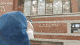 a person wearing a mask stands in front of a building that has chinese writing on it