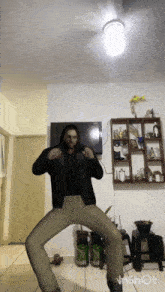 a man in a black jacket and khaki pants is dancing in front of a television