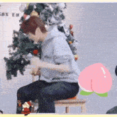 a man in a grey hoodie sits on a chair in front of a christmas tree ..