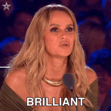 a woman is speaking into a microphone and the word brilliant is on the screen behind her