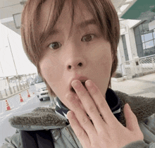 a person covering their mouth with their hand while wearing a jacket