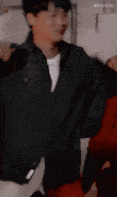 a man wearing a black jacket and a white shirt is standing in front of a wall .