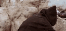 a person in a hooded cloak is standing in front of a rock wall .