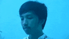 a young man is standing in front of a blue background and looking at the camera .