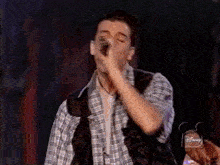 a man singing into a microphone while wearing a plaid shirt and a black vest