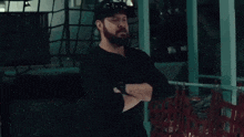 a man with a beard and sunglasses is standing with his arms crossed in a room .