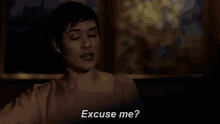 a woman is sitting in a dark room talking to someone and says `` excuse me ? ''