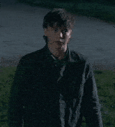 a young man wearing a black jacket stands in a field