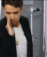 a man wearing a black jacket and a gold chain is covering his nose with his hand