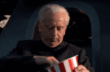 a man eating popcorn from a red and white striped bucket
