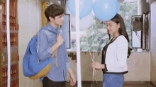 a boy and a girl are standing next to each other in a room holding balloons .