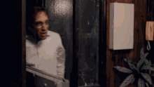 a man wearing glasses is standing in a doorway looking out a window