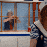 a woman in a sailor hat looks out a window at another woman