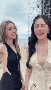 two women are standing next to each other on a beach with their eyes closed and smiling